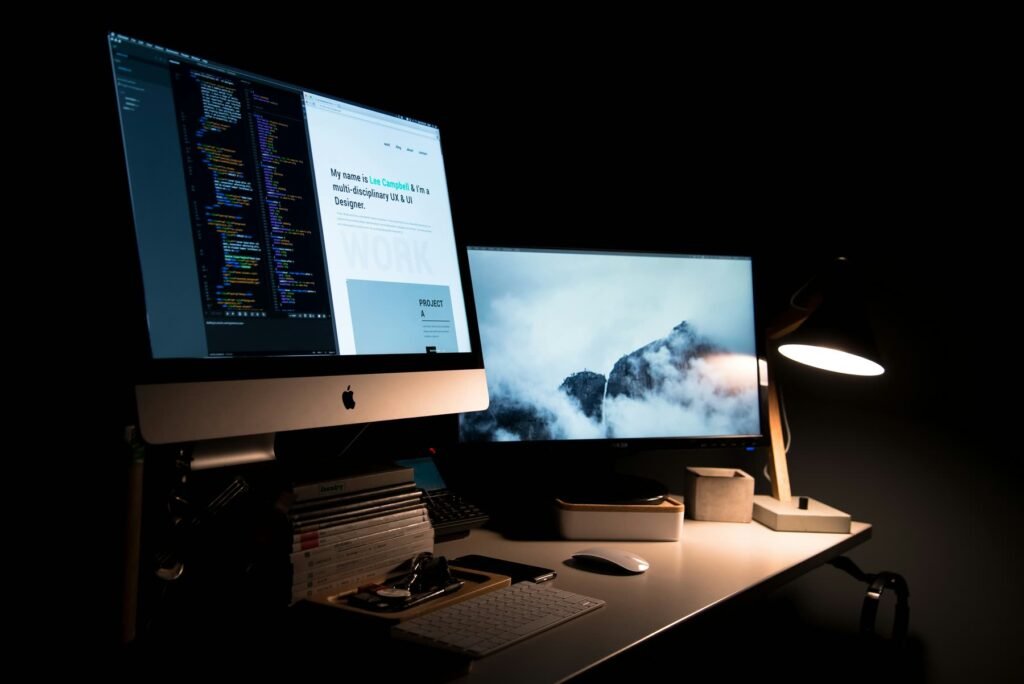 Designer's desk at night with a monitor showing website code and a portfolio page